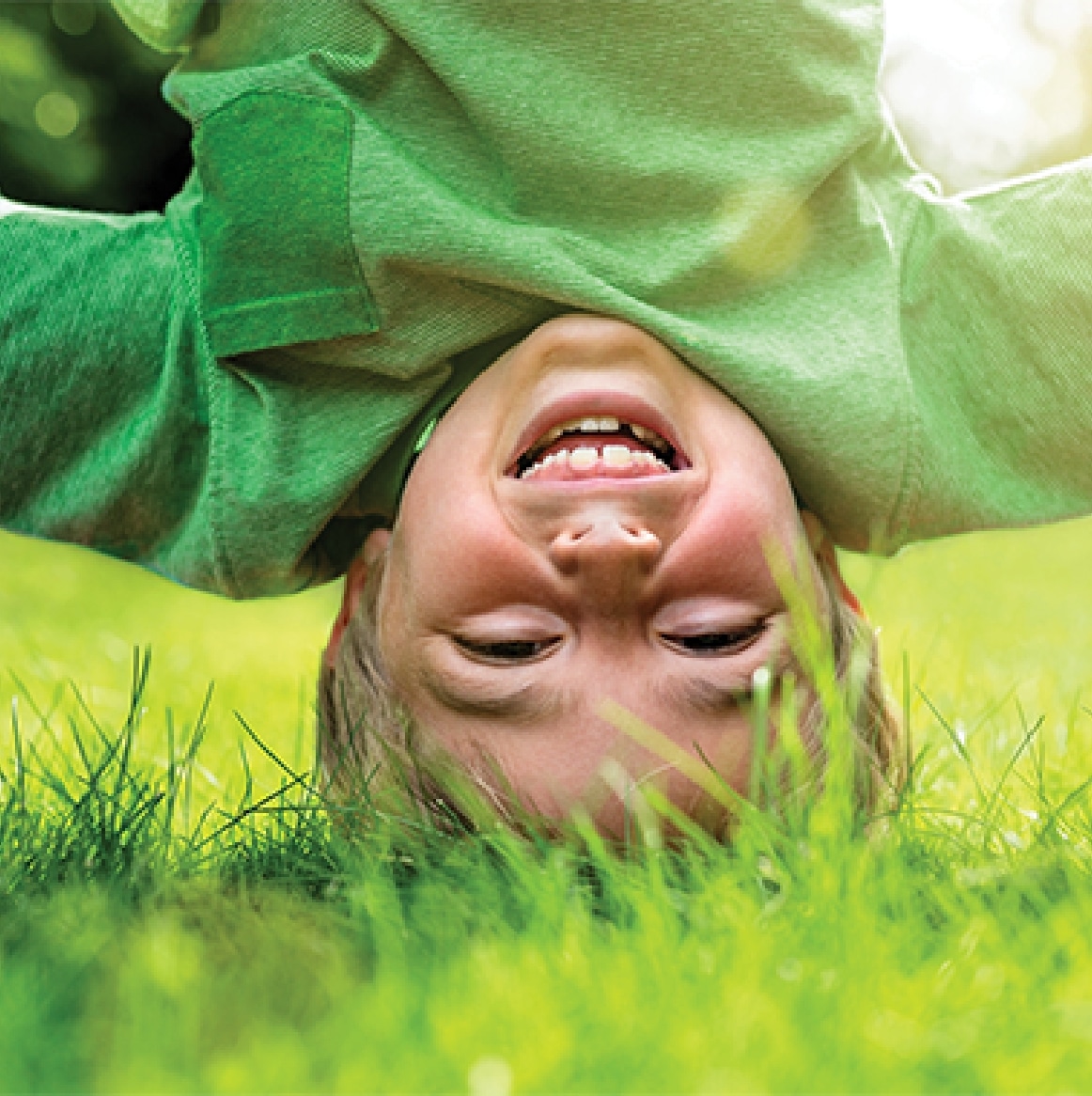 Child playing upside down on a grassy lawn, smiling and enjoying the outdoors.