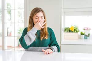 "Young woman at a kitchen table pinching her nose to avoid a bad smell, emphasising the removal of poo odours.