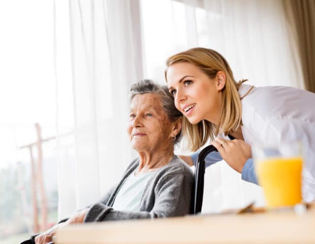 A photo of an elderly lady in a wheelchair looking happy, with a younger lady talking to her.