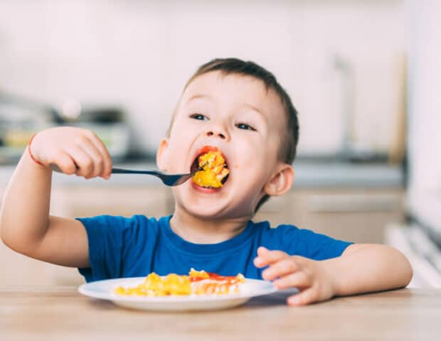 oung boy in a blue shirt eating a plate of fried food in a kitchen, illustrating the need to eliminate lingering fried food odours.