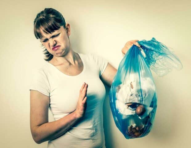 "Woman holding a smelly blue rubbish bag, reacting with disgust.