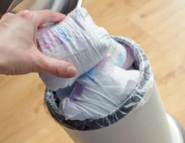 Woman hand put used diaper to the Trash bin full of used diapers. Close up.