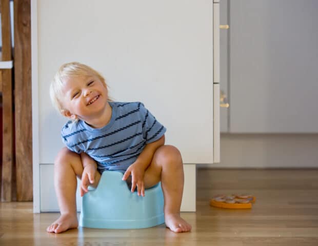 Little toddler boy, sitting on potty, playing with wooden toy