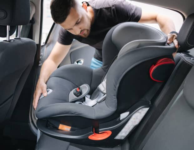 Man installs a child car seat in car at the back seat. Responsible father thought about the safety of his child
